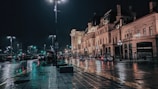 A city street scene at dusk, with neon lights reflecting on wet pavement.