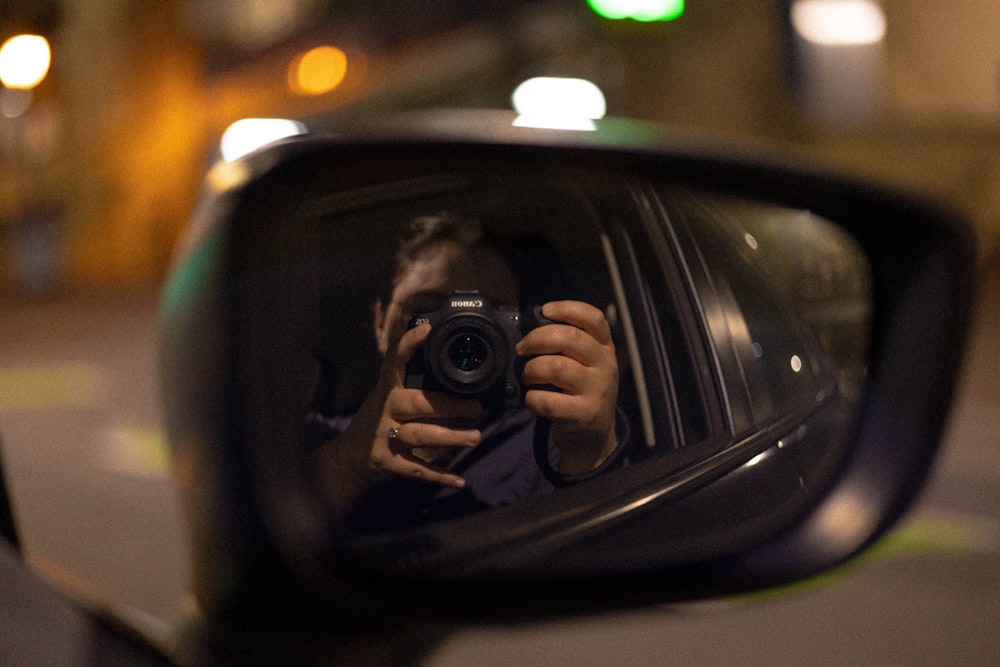 a woman taking a picture of herself in a car mirror