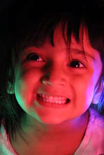 A cheerful child confidently speaking on stage with colorful lighting and a smiling audience.