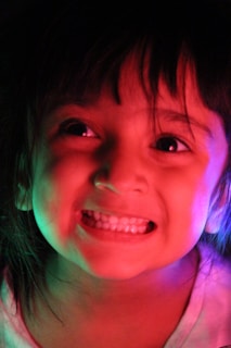A close-up of a child's smiling face with Christmas lights in the background.