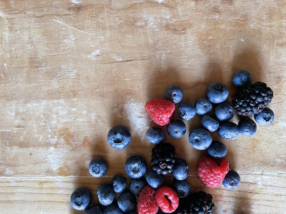 A collection of mixed berries, including blueberries, raspberries, and blackberries, are scattered on a rustic wooden surface.
