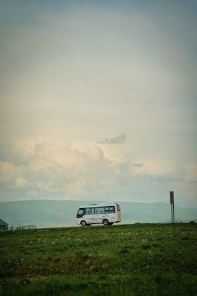 A scenic countryside field trip with a Safetrip Coaches minibus parked nearby and children exploring.