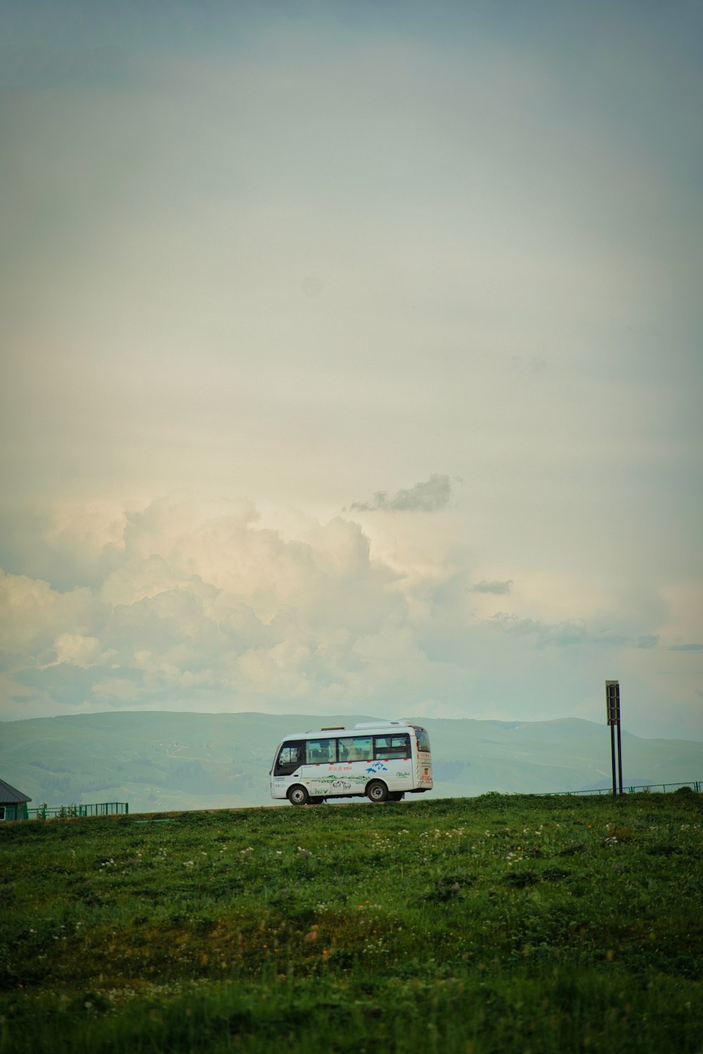 a white bus driving down a road next to a lush green field