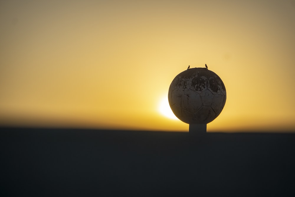 the sun is setting behind a globe on top of a pole