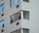 A close-up view of a multi-story residential building facade with white brick walls and several windows. Some windows have air conditioning units installed below them.