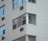 A close-up view of a multi-story residential building facade with white brick walls and several windows. Some windows have air conditioning units installed below them.