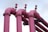 Four large pink industrial pipes extend upward, each with a valve on top, set against a light blue sky.