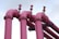 Four large pink industrial pipes extend upward, each with a valve on top, set against a light blue sky.