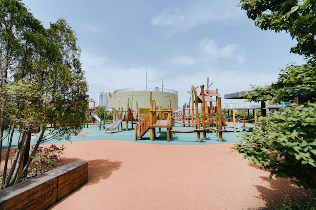 A wide shot of a natural wooden playground integrated into a park with trees and benches.