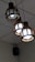 Three spherical pendant lights with wooden frames hanging from the ceiling, emitting a white glow. The ceiling is composed of white panels, and a black speaker is mounted in the corner.