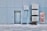 A blue tiled wall with a closed metal door and several air conditioning units mounted above and beside it. Next to the AC units is a red hose cabinet with a fire safety sign.