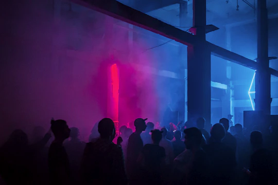A lively party scene with colorful neon signs lighting up the space in blue and purple hues.