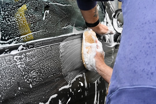 A close-up of a hand carefully washing a shiny car door with a soft sponge.