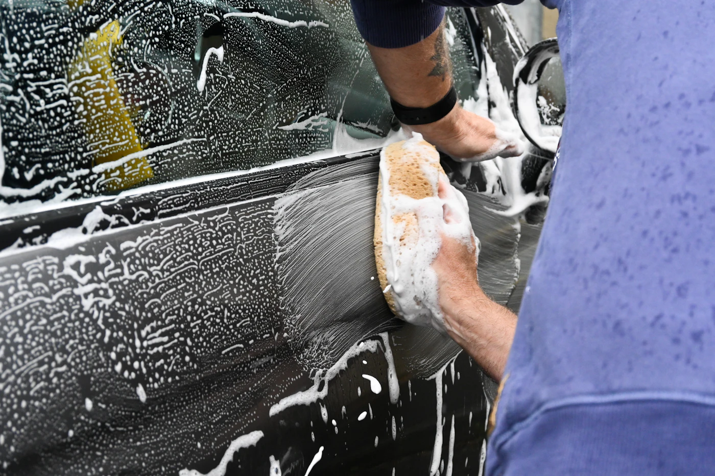 Detailer hand-washing a car with foam and sponge