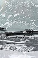 A windshield covered in soapy water and foam, with a windshield wiper visible in the image.