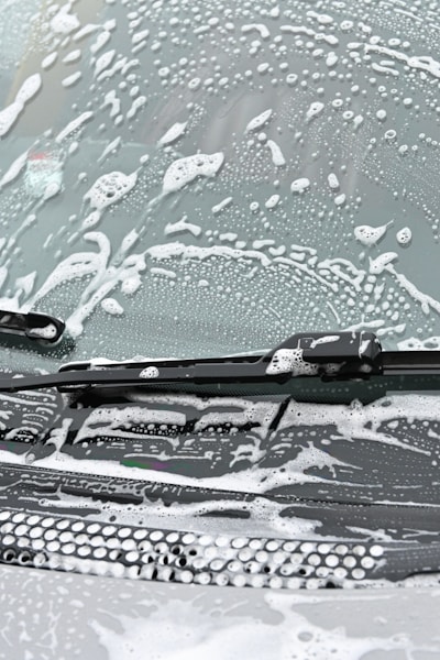 A windshield covered in soapy water and foam, with a windshield wiper visible in the image.