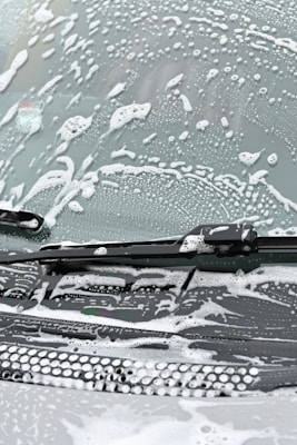 A windshield covered in soapy water and foam, with a windshield wiper visible in the image.