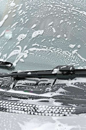 A windshield covered in soapy water and foam, with a windshield wiper visible in the image.