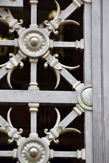An intricate wrought iron grate featuring symmetrical designs with circular and floral motifs. The metalwork includes elegant curves and decorative elements, combining function with artistic expression.