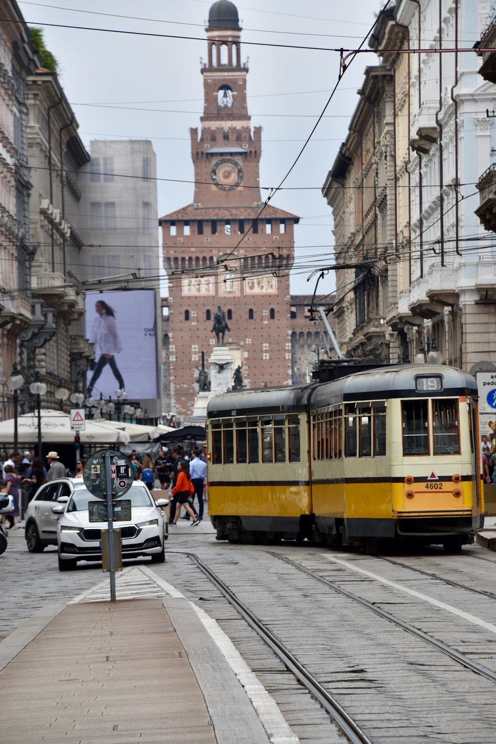 a yellow and black train traveling down a street next to tall buildings