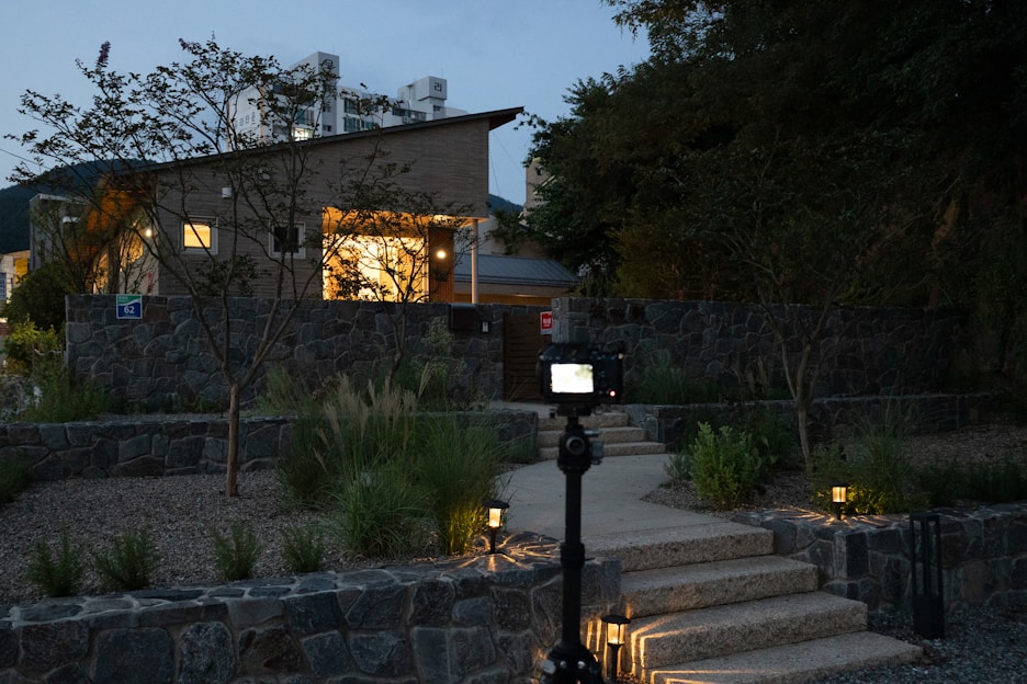 A sleek smart CCTV camera mounted on a modern home exterior at dusk, softly illuminated by porch lights.