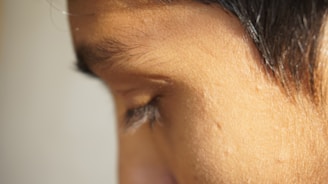 A close-up of a person's face focusing on the eye area, capturing fine details such as eyelashes, skin texture, and hair. The lighting highlights the natural complexion and contours.
