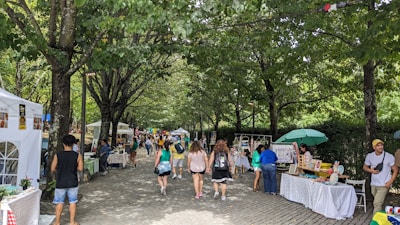 Visitors strolling along a shaded market path lined with artisan booths and lush greenery.