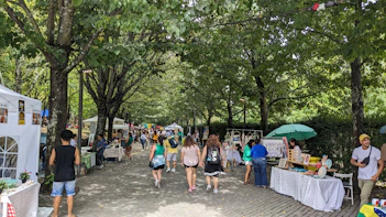 Shoppers browsing a lively market street lined with farm stalls and colorful produce.