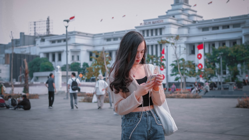 a woman standing in front of a building looking at her cell phone