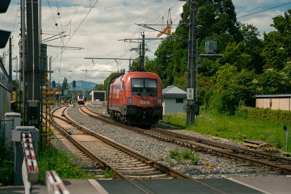 a red train traveling down train tracks next to a forest