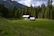 Cozy alpine cabin surrounded by lush green forest under a clear blue sky.