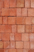 A neatly stacked arrangement of uniform red bricks arranged in a tight pattern covering the entire frame. The bricks vary slightly in hue and texture, giving the arrangement a somewhat rustic and natural appearance.