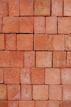 A neatly stacked arrangement of uniform red bricks arranged in a tight pattern covering the entire frame. The bricks vary slightly in hue and texture, giving the arrangement a somewhat rustic and natural appearance.