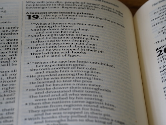 An open Bible displaying a page from the Book of Ezekiel with text about a lament over Israel's princes. The scripture includes numbered verses and is written across both visible pages.