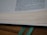 A close-up of an open book with visible text and neatly aligned pages. Two green ribbon bookmarks extend from the bottom, resting on a wooden surface.