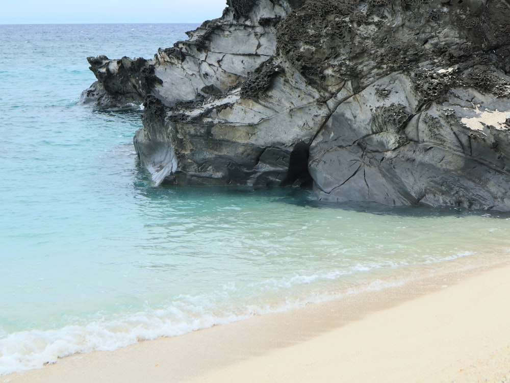 a sandy beach next to a large rock formation