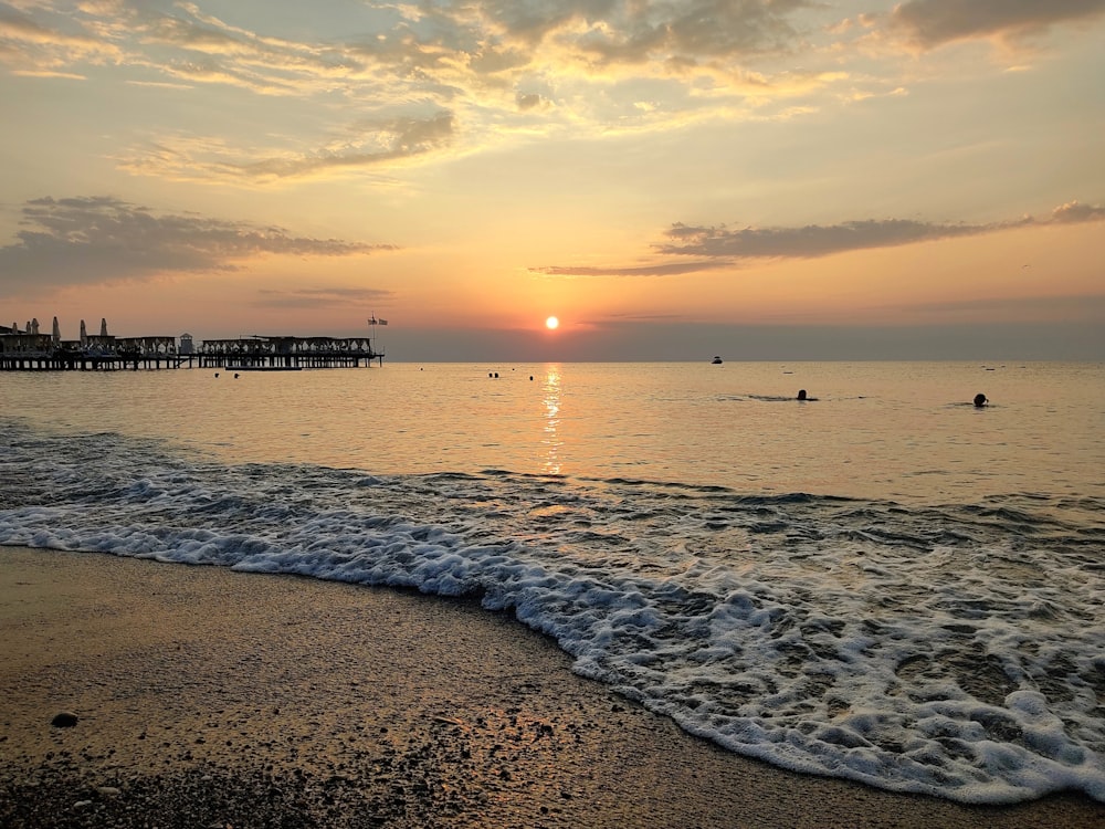 a sunset over the ocean with people swimming in the water