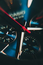 Close-up view of an intricate watch face featuring multiple dials and a vibrant red second hand. The watch has a metallic finish with visible branding.