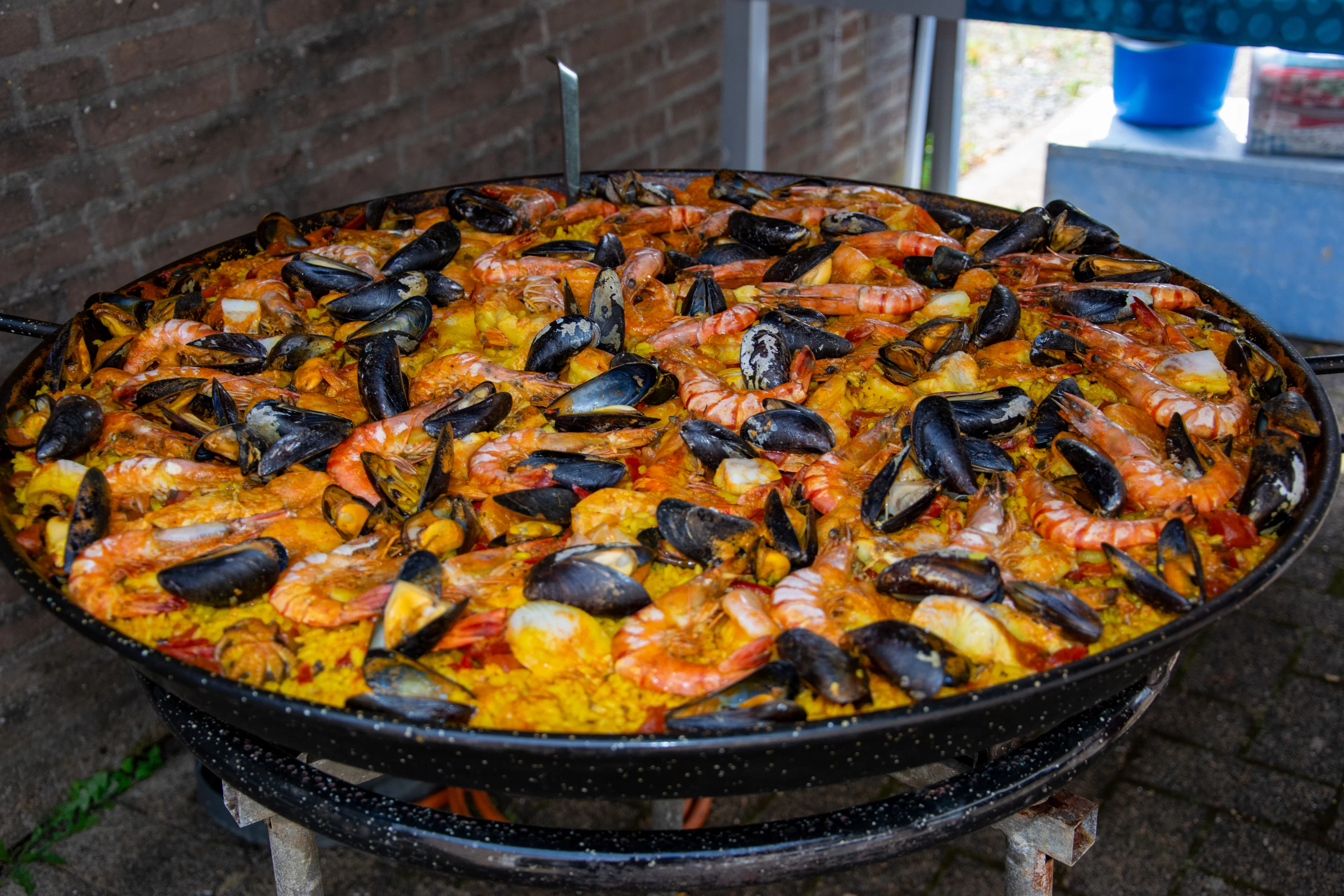 Large seafood paella with mussels and prawns cooking over an open fire