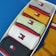 A set of folded socks in different colors arranged neatly in a box. Each sock features a detailed pattern with vibrant stripes, including elements of red, white, and blue, against background colors of grey, yellow, mint, white, and black.