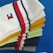 A collection of colorful socks neatly stacked on top of a blue surface. The socks display a variety of colors including white, yellow, green, black, and gray, each featuring a red and navy blue striped pattern. One sock has a small embroidered logo.