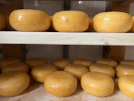 Freshly made donkey milk cheese wheels resting on wooden shelves in a sunlit room.