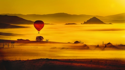 An elegant hot air balloon floating over misty mountains during sunrise, painted in warm golden hues.