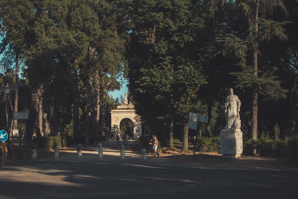 a statue in the middle of a road surrounded by trees