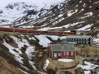 a red train traveling down tracks next to a snow covered mountain