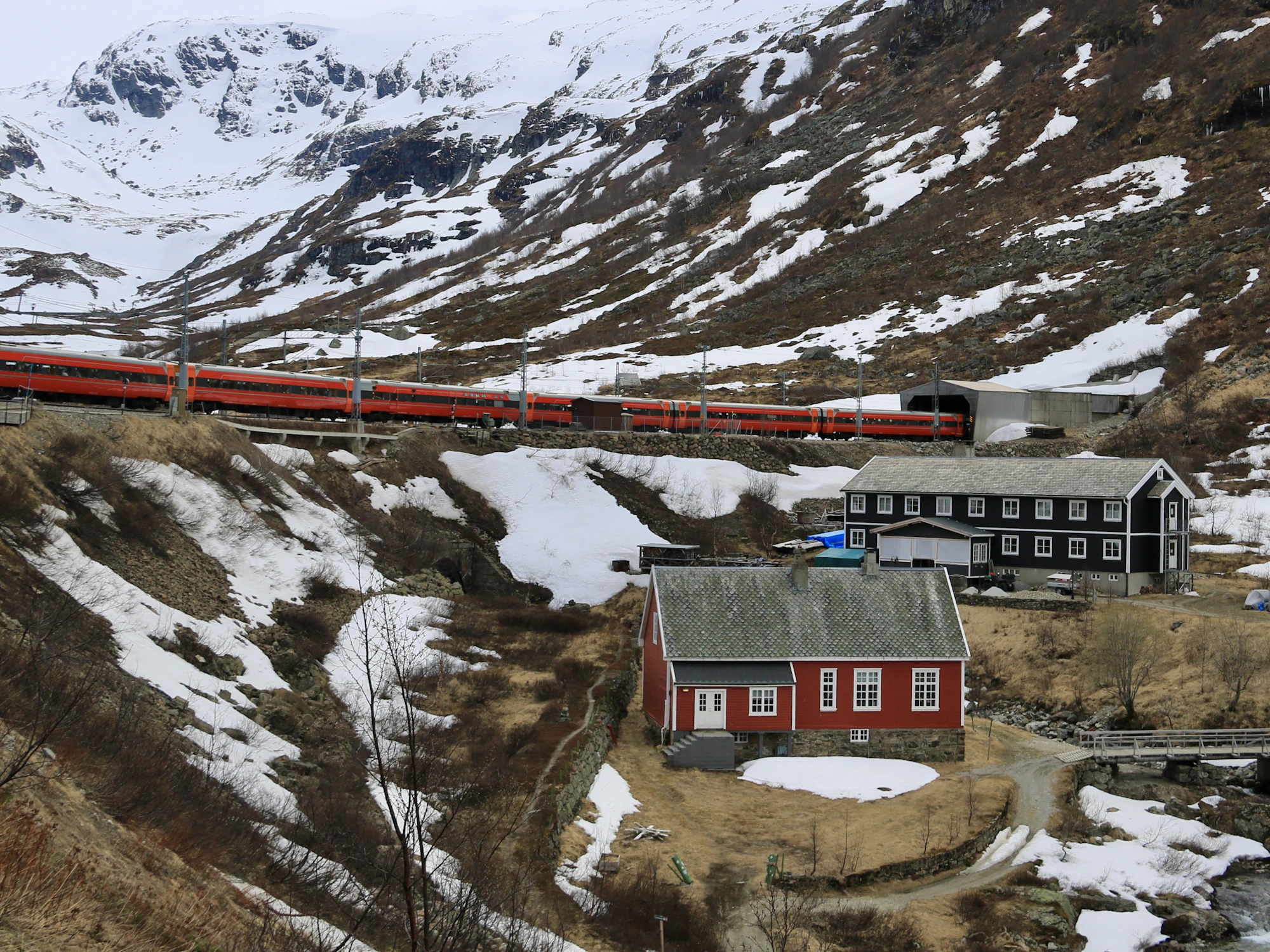 A red train crossing a snowy mountain landscape above a red house
