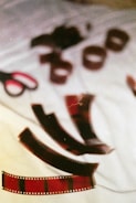 A scattered arrangement of film negatives lies on a white cloth surface. A pair of scissors with red and black handles is nearby, adding to the artistic and nostalgic theme. The scene appears to be a casual setting, possibly a creative workspace.
