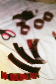 A scattered arrangement of film negatives lies on a white cloth surface. A pair of scissors with red and black handles is nearby, adding to the artistic and nostalgic theme. The scene appears to be a casual setting, possibly a creative workspace.