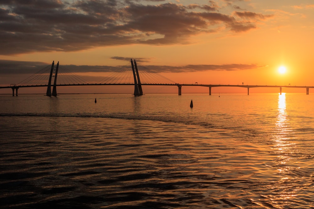 the sun is setting over the water with a bridge in the background