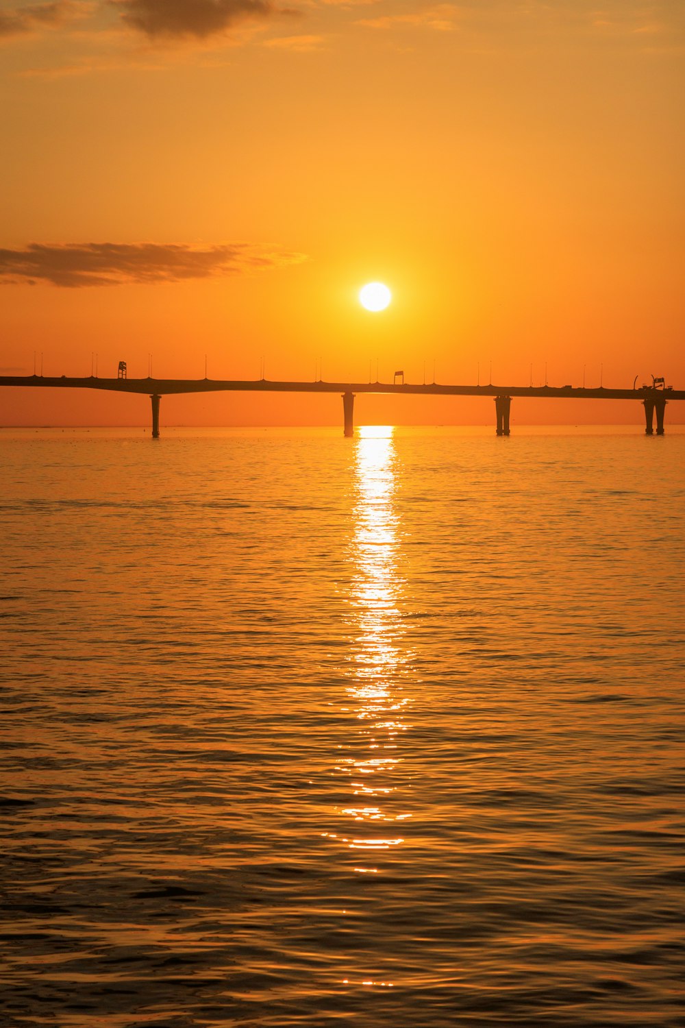 the sun is setting over the water with a bridge in the background